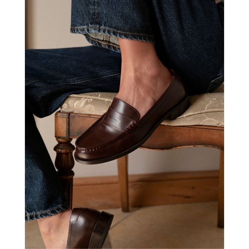 Burgundy leather penny loafers with a polished finish, classic moccasin stitching, and a low stacked heel. A timeless staple for effortless sophistication.