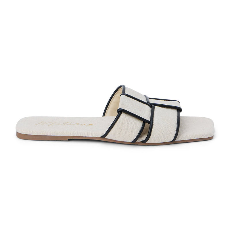 Chic flat slide sandals in an ivory fabric with black-trimmed crisscross straps. Featuring a square toe and minimalist design, these sandals are perfect for effortless summer style.