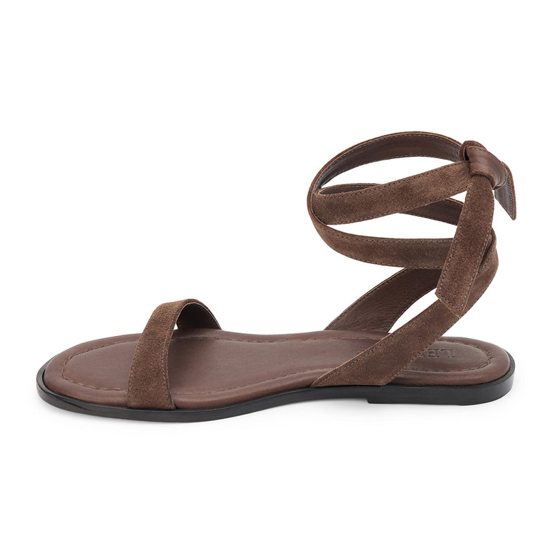 Café suede flat sandal with delicate straps and a secure ankle tie. A minimalist and feminine silhouette, perfect for effortless warm-weather styling.