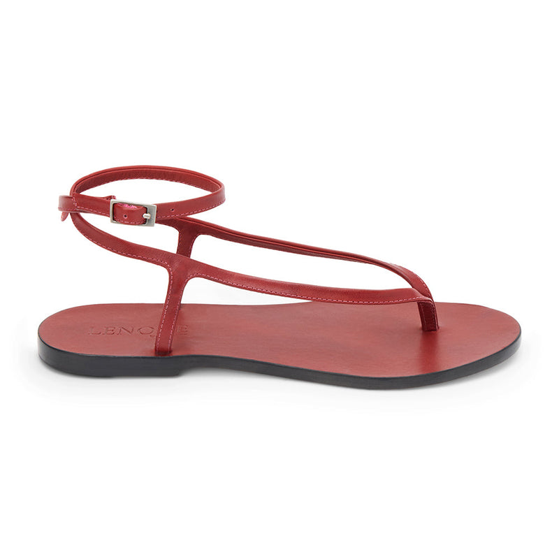 Cherry red leather thong sandal with a minimalist strappy design and adjustable ankle buckle. A sleek and versatile style for effortless warm-weather dressing.