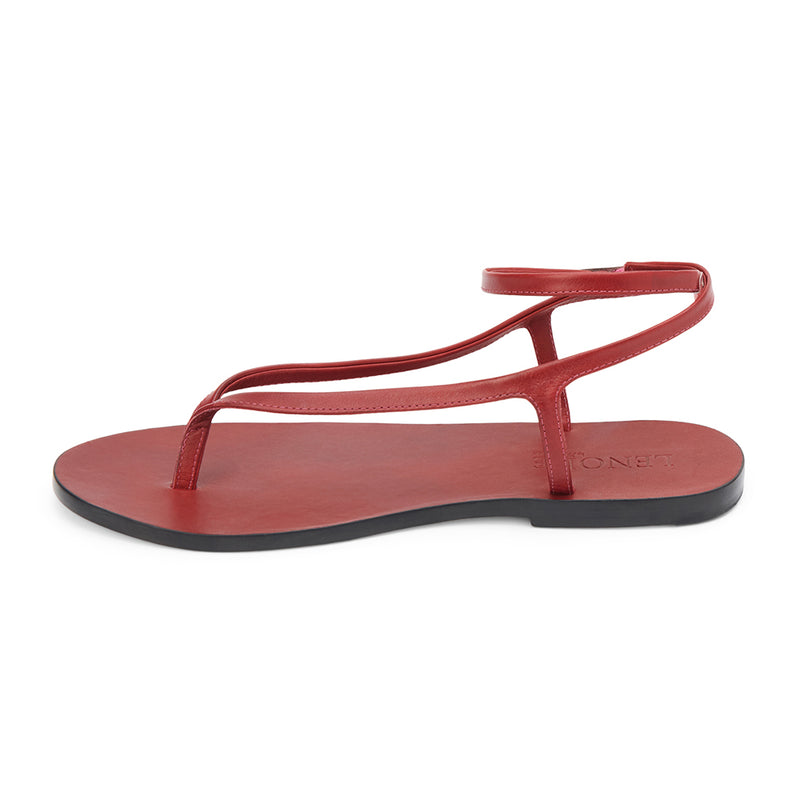 Cherry red leather thong sandal with a minimalist strappy design and adjustable ankle buckle. A sleek and versatile style for effortless warm-weather dressing.