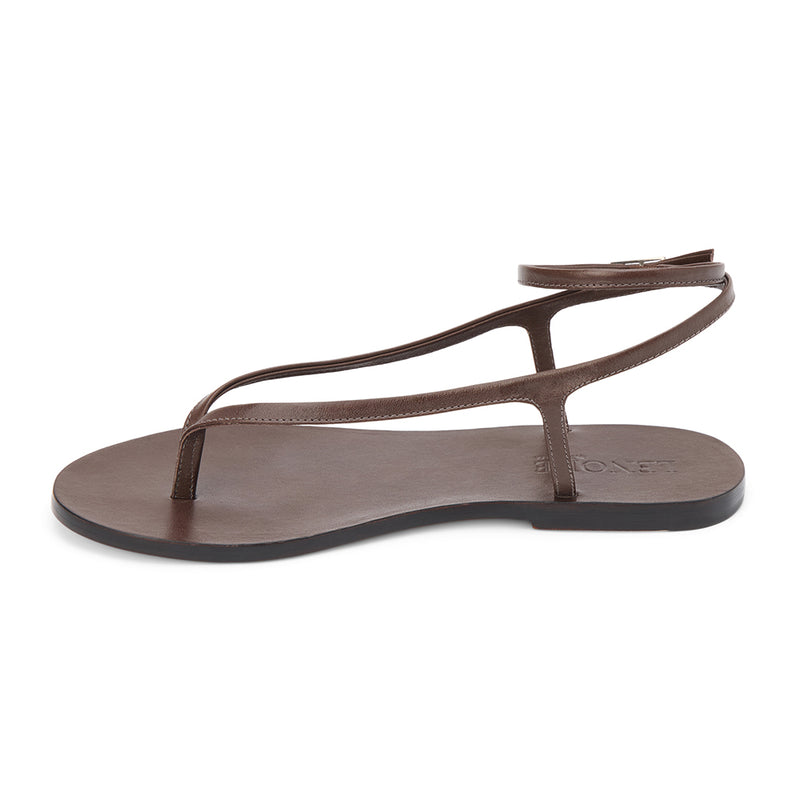 Dark brown leather thong sandal with a minimalist strappy design and adjustable ankle buckle. A sleek and versatile style for effortless warm-weather dressing.