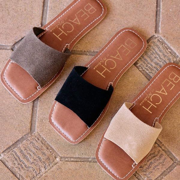 Three pairs of the Bali slide sandal in neutral tones (dark brown, black, and cream) with a wide single strap and comfortable flat soles, perfect for relaxed summer days.