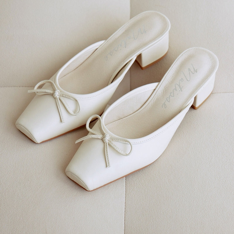 Pair of white mule heels with square toes and a delicate bow accent. These stylish heels feature a low block heel for comfortable all-day wear.