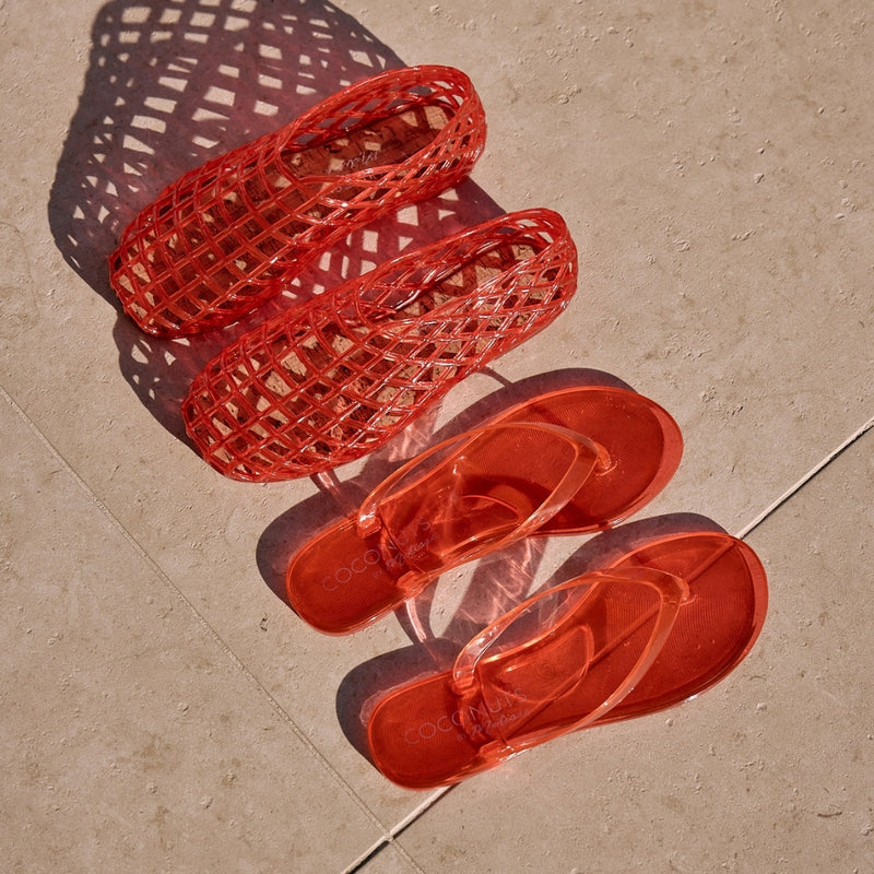 Red jelly flip-flops and woven flats with transparent straps and a minimalist design. A lightweight, water-friendly essential for effortless summer wear.